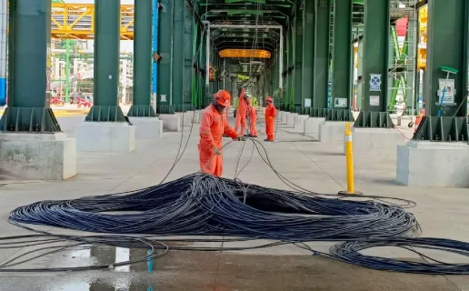 Workers handling large coiled cables in an industrial setting.