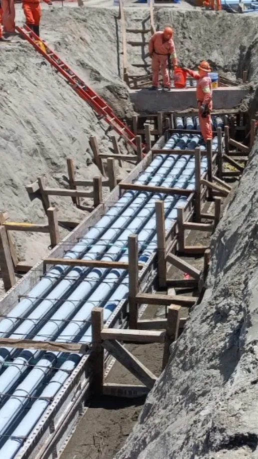 Construction workers installing large blue pipes in a deep trench.