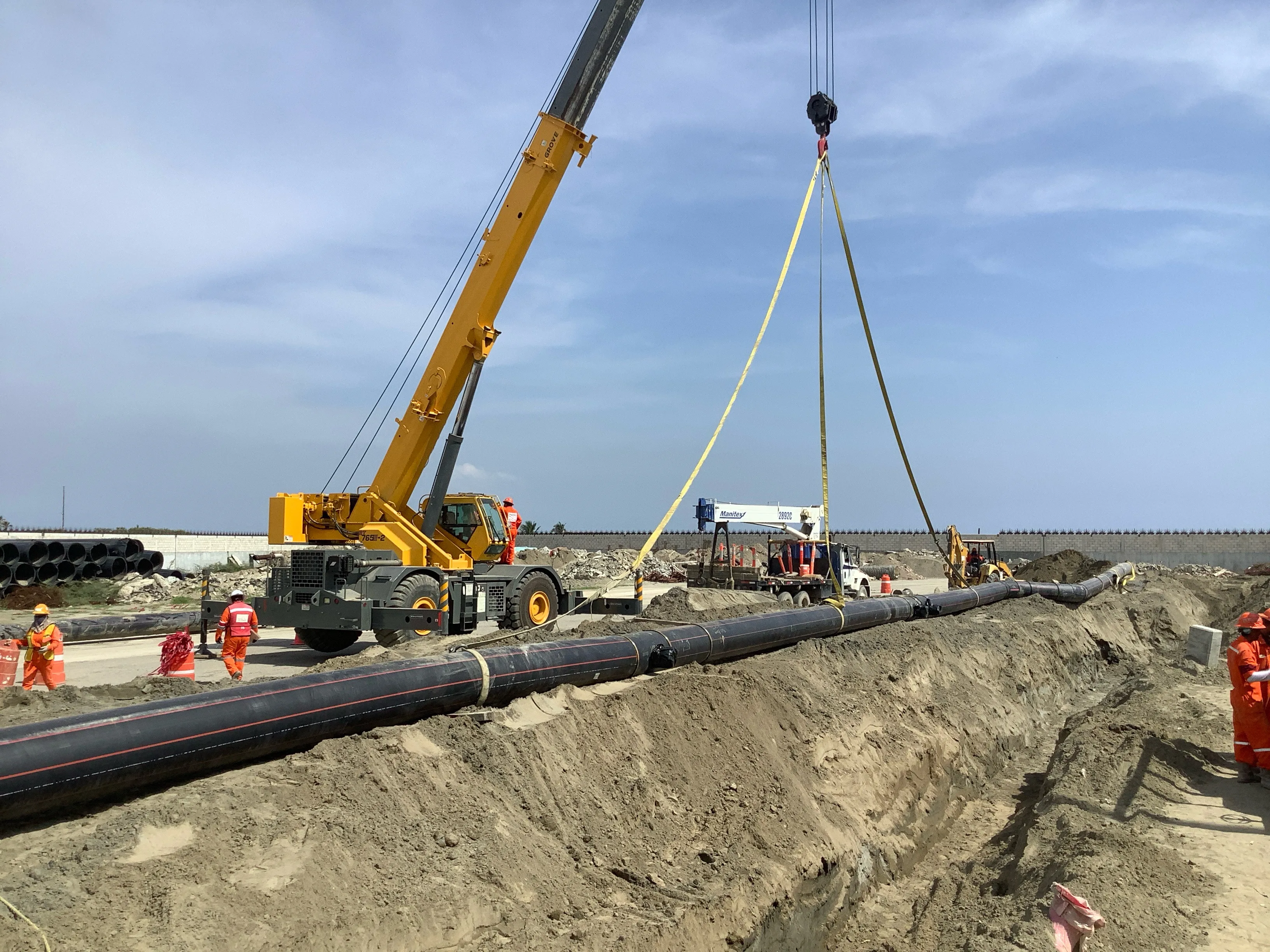 Construction site with workers installing a large pipeline lifted by a crane.