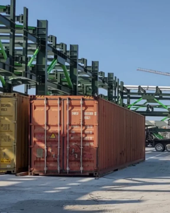 Shipping containers on a concrete surface with steel framework under a clear sky.